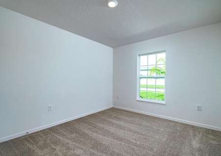 Carpeted spare bedroom with a window overlooking the front yard. 