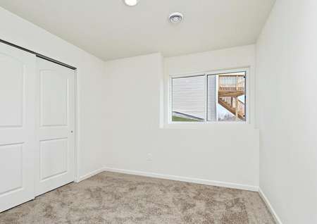Lower level bedroom of split-level home with window overlooking backyard and sliding doors on closet.