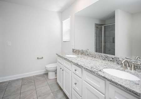 A bathroom in the Kiawah floor plan with tile flooring, double sink vanities, granite countertops and white cabinets. 