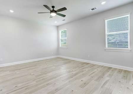 Expansive master bedroom with wood flooring, a ceiling fan, and two windows to allow natural light to flow in.