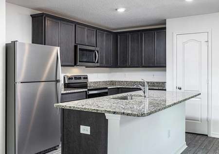 Full kitchen with installed appliances, granite countertops and upper-wood cabinets with crown molding.