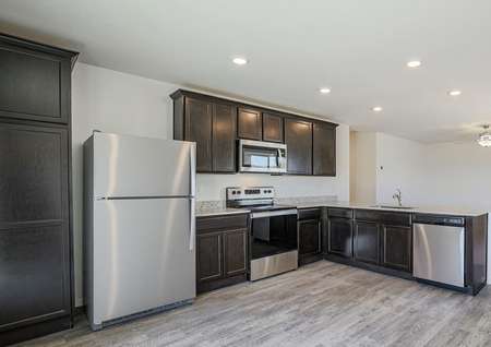 Open kitchen with stainless steel appliances and dark cabinets.