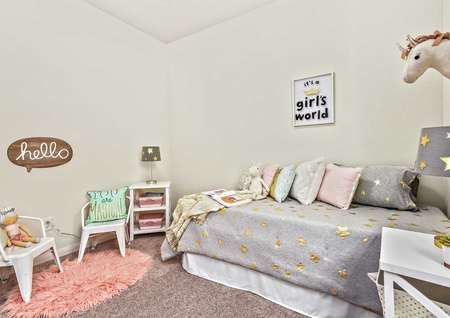 Kid's bedroom that has multi-colored pillows, a white dresser with books and a lamp with gold stars on the shade.