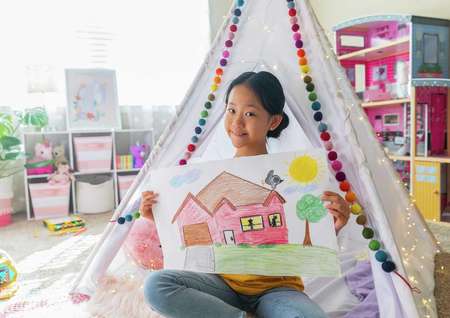 Stock image of girl in her bedroom coloring a picture of a house.