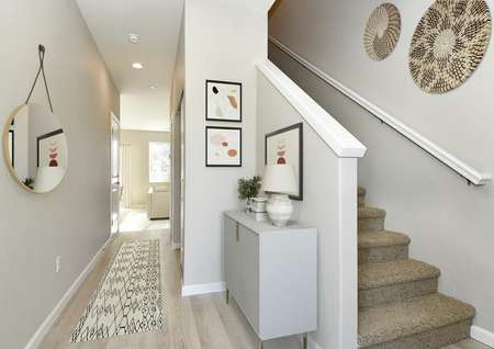 Entryway with natural light, a storage console with a lamp on top, artwork collection and a runner rug leading to the living room.