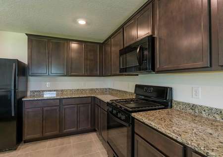 Cocoa plan's kitchen with granite countertops, brown cabinets, tile flooring and all black appliances.