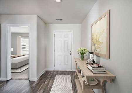 Staged entryway with rug and side table with view of secondary bedroom.