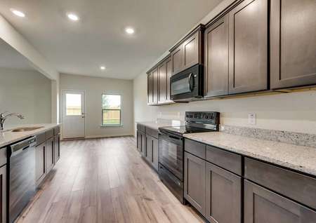 Oakmont kitchen with vinyl flooring and dark brown custom cabinets, black appliances and recessed lighting 