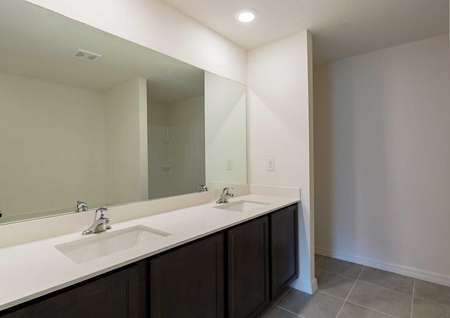 A tile-floored bathroom in the Estero floor plan with white double sink vanities and quartz countertops.