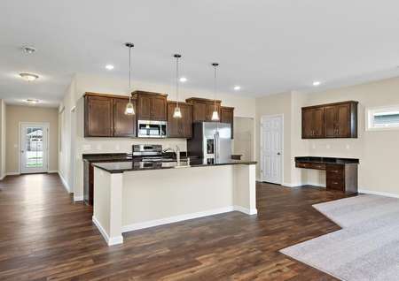 Photo of kitchen with brown cabinets, plank flooring, stainless appliances and an island with pendant lights over it.