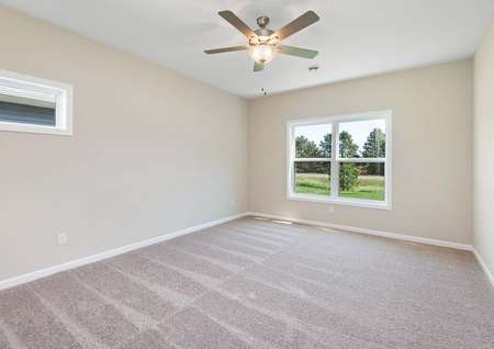 Photo of the primary bedroom with carpet and ceiling fan and large window overlooking the back yard.