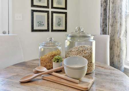 Walnut staged home with two large glass cereal jars, wooden spoon and cutting board, and white bowls on the kitchen table
