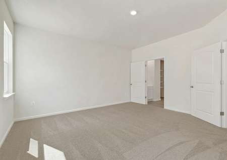 Spacious master bedroom with recessed light, beige carpet, window, view into attached bathroom.