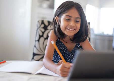 Stock photo of a cute elementary age girl using a laptop computer while attending school online.