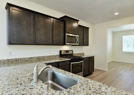Kitchen with granite breakfast bar, single basin sink and dark brown cabinetry.