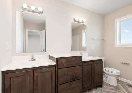 Photo of a spacious bathroom with two vanities connected by a raised countertop, herringbone inlaid plank flooring and a window.