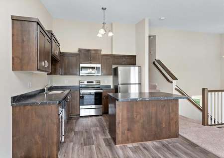 Photo of the open and spacious kitchen in the Blackberry townhome by LGI Homes, complete with LVP flooring, an island with barstool seating, stainless steel appliances and dark brown cabinets.