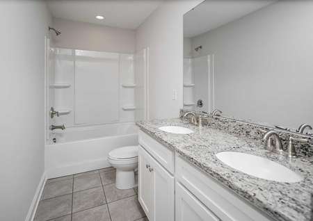 A tile-floored bathroom in the Kiawah floor plan with white cabinets, two-sinks and granite countertops.