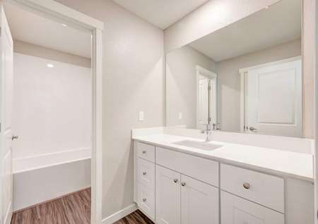 A bathroom in the Empire floor plan with marble countertops, white cabinets and a door leading to the tub and toilet.