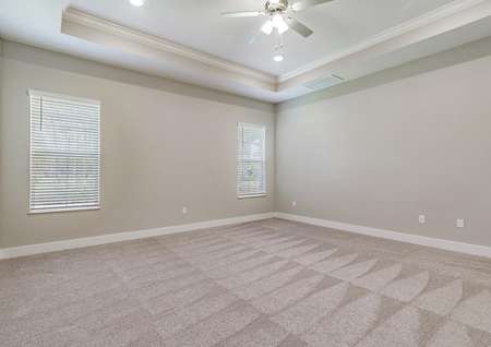 Master bedroom with carpet, two windows, tall ceilings and a fan.