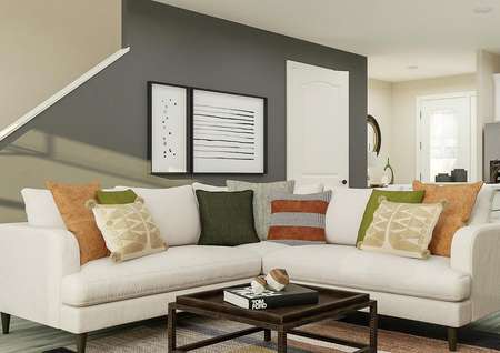 Rendering of living room showing white
  sectional couch, metal coffee table, and grey accent wall behind along with
  kitchen in background with wood look flooring throughout.