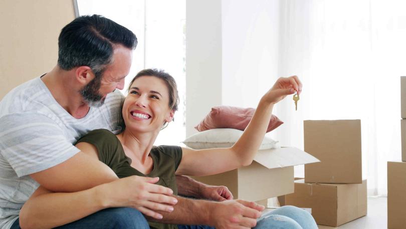 Happy middle-aged couple sitting on floor near moving boxes holding keys