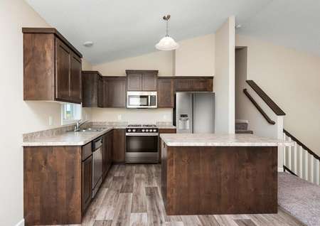 Photo of a kitchen with brown cabinets, light brown counters, light plank flooring, stainless steel appliances and an island.