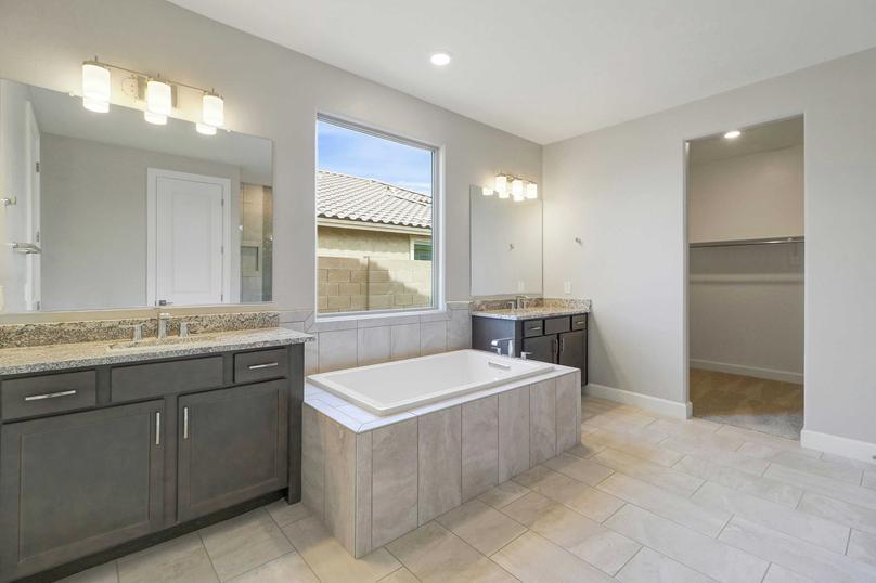 Hawley master bath with two granite vanities, brown cabinetry, and large framed-in bathtub