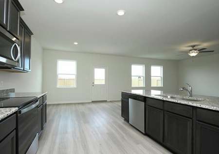 Photo of kitchen with dark brown cabinets, granite counters, light gray plank flooring looking into adjacent dining and living rooms.
