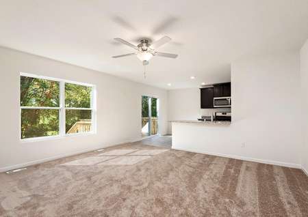 Spacious living room with carpet and ceiling fan and window overlooking the back yard.