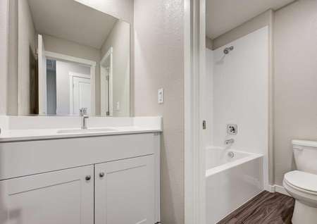 A bathroom with a sink, white cabinets, a bath/shower combo and wood-like flooring in the Loomis floor plan.