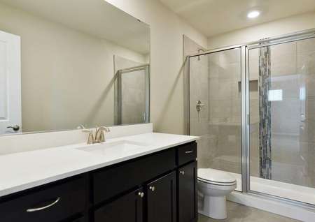 The Northwest Cypress bathroom is shown with a walk in glass shower and white quartz sink countertop and dark brown cabinets.