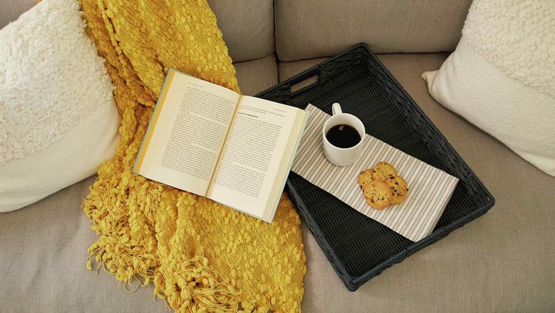 Staged living room with book, coffee cup, and yellow shawl on couch.