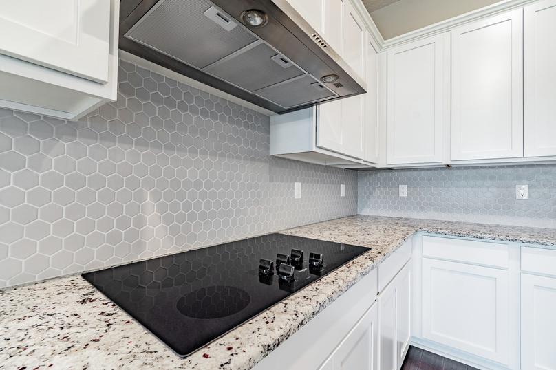 Kitchen with granite countertops, white cabinetry and a grey backsplash. 
