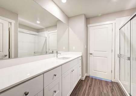 The master bathroom in the Empire floor plan that has white cabinets, recessed lighting and vinyl wood-like flooring.
