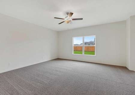 The spacious living room in the Rio model. Carpet flooring a ceiling fan and large window are in the picture