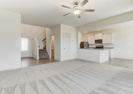Large living room with carpet and ceiling fan looks toward foyer and staircase. breakfast bar and into kitchen.