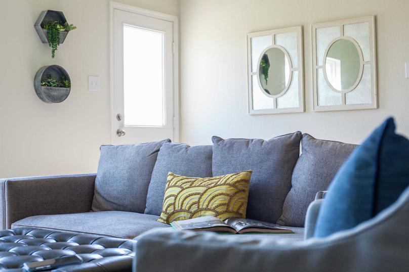 Staged living room with blueish grey couch that has a green and brown pillow on it and two framed mirrors hanging on the wall in the background