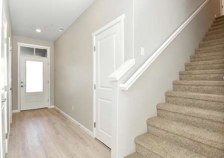 Welcoming entryway with glass front door, plank flooring, carpeted stairway.