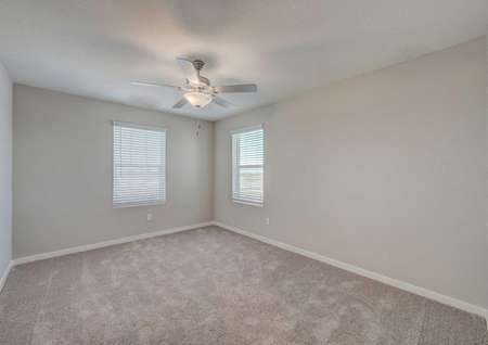 Secondary bedroom in the Loomis floor plan with light brown carpet, tan walls, white baseboards and a ceiling fan.