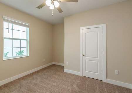 Carpeted spare bedroom with a ceiling fan and large window. 