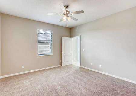 The Mateo model home's master bedroom. Tan walls, white baseboards, a ceiling fan and tan carpeting
