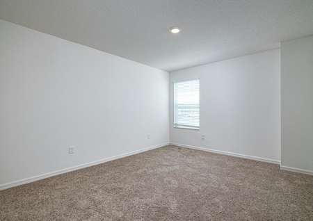 Spacious bedroom with carpet, recessed lighting and a window with natural light entering the room.