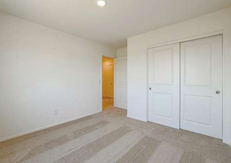 Secondary bedroom with tan carpet and closet with sliding doors.