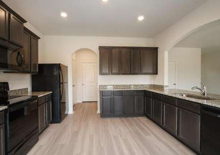 Vinyl wood-like floors, dark brown cabinets, granite counters, and black appliances in the Rayburn floor plan kitchen