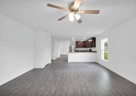 Elongated family room with a ceiling fan and a view of the chef-ready kitchen.