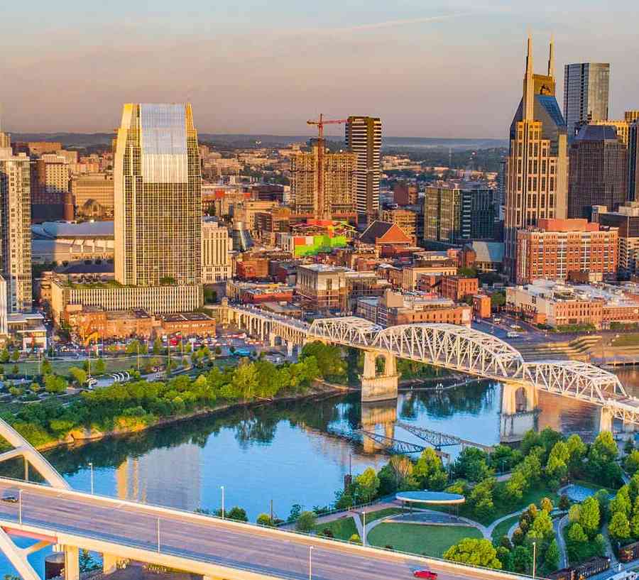 Nashville, Tennessee skyline showing bridges crossing the Cumberland River, downtown city buildings, and blue skies on the horizon