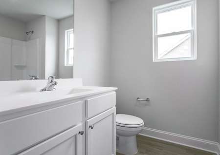 Secondary bathroom with vinyl flooring and white cabinets.