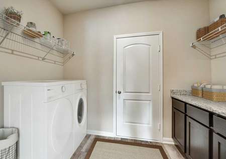 Staged Oakmont laundry room with washer and dryer, upper shelves, granite countertops on brown cabinets and white entry door