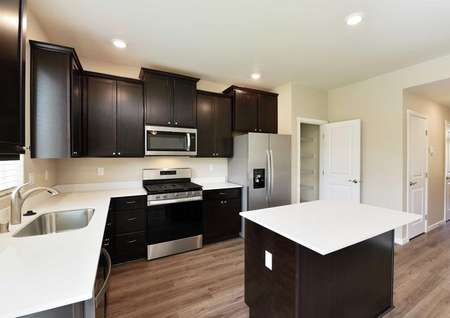 The Northwest Cypress kitchen is shown with dark brown cabinets and white quartz countertops and a kitchen island.